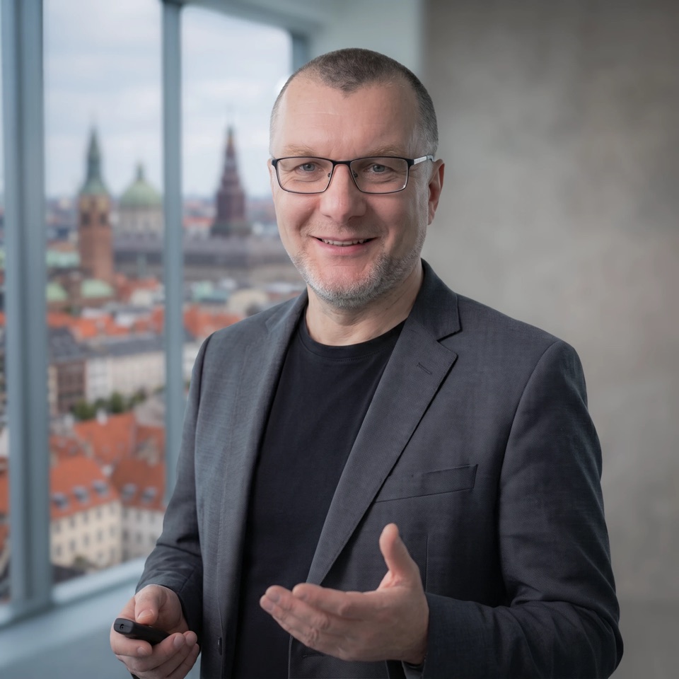 Pavel Bukengolts smiling and gesturing by a window overlooking a city skyline